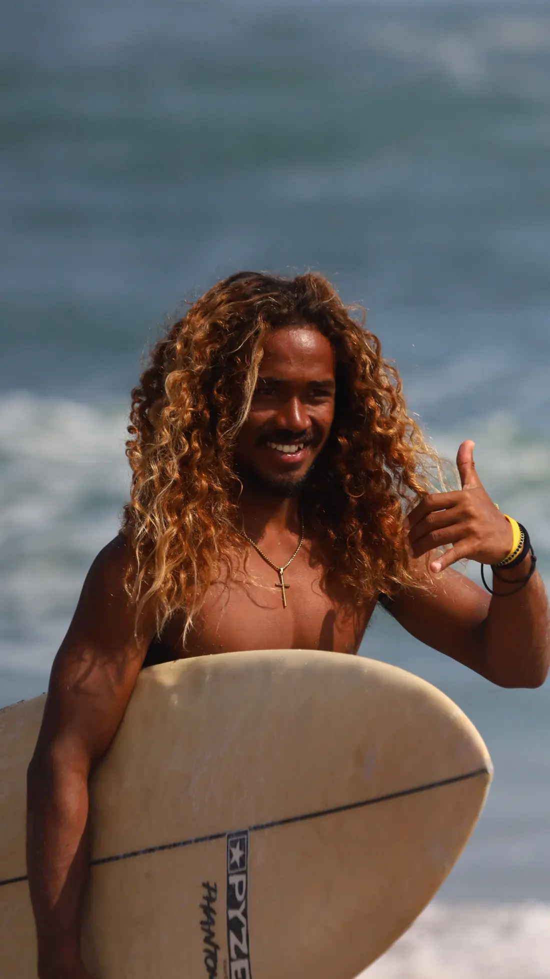 Gervas, surf instructor in Canggu, holding his surfboard and throwing a shaka